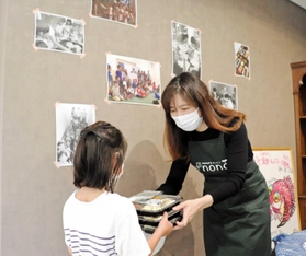 手作り弁当を子どもに手渡すスタッフ。壁には過去の写真が飾られている=明石市小久保6 手作り弁当を子どもに手渡すスタッフ。壁には過去の写真が飾られている=明石市小久保6