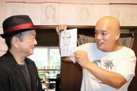 描いた似顔絵を来店客に見せる神代さん(右)=洲本市下加茂2 描いた似顔絵を来店客に見せる神代さん(右)=洲本市下加茂2