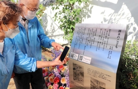完成した碑を眺める脇村さん(右)と、歌を聴くためのQRコードにスマートフォンをかざす、願う会メンバーの紀田知美さん=洲本市栄町4 完成した碑を眺める脇村さん(右)と、歌を聴くためのQRコードにスマートフォンをかざす、願う会メンバーの紀田知美さん=洲本市栄町4