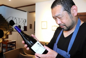 小谷さんの畑でとれたブドウで試験醸造したワインを手にする井壷さん=洲本市山手1 小谷さんの畑でとれたブドウで試験醸造したワインを手にする井壷さん=洲本市山手1