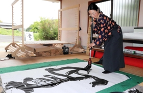巨大な和紙の上で筆を進める束田裕美さん=洲本市五色町都志大日 巨大な和紙の上で筆を進める束田裕美さん=洲本市五色町都志大日