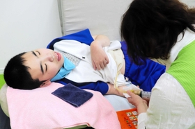看護師の処置で栄養剤を摂取する浜晃生さん(左)=洲本市物部3 看護師の処置で栄養剤を摂取する浜晃生さん(左)=洲本市物部3
