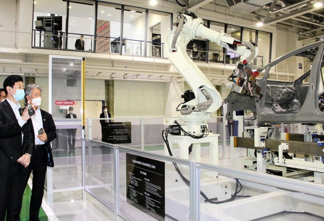 自動車の組み立て用ロボットが並ぶショールームを視察する西村康稔経済産業相(手前)=11日午前、神戸市西区櫨谷町松本、川崎重工業西神戸工場