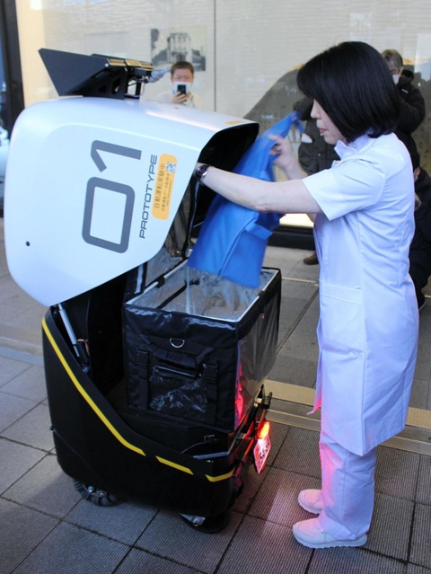 病院前で配送ロボットに医薬品を詰め込む看護師=東京都新宿区