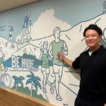 神戸の風景とアウトドアを楽しむ人たちを描いた壁と長尾洸太朗社長=神戸市中央区脇浜海岸通1