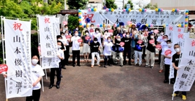 横断幕の前で山本俊樹にエールを送る地元住民ら=三木市緑が丘町中1 横断幕の前で山本俊樹にエールを送る地元住民ら=三木市緑が丘町中1