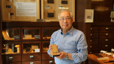 伝統の手作りの刷毛が並ぶ江戸屋の店内で、うるし刷毛を手に解説する●田捷利さん=中央区日本橋大伝馬町2※●は「浜」の異体字