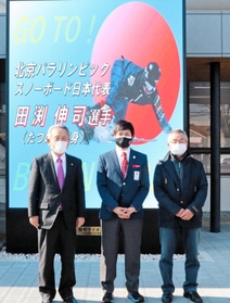 大型ビジョンに流れる応援メッセージを背に、山本実市長(左)に意気込みを語った田渕伸司選手(中央)と父の建次さん=たつの市役所 大型ビジョンに流れる応援メッセージを背に、山本実市長(左)に意気込みを語った田渕伸司選手(中央)と父の建次さん=たつの市役所