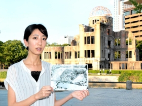 ピースボランティアの松本愛美さん。「平和記念公園は、昔は中島地区という住宅街だった」と写真を持って説明する=広島市中区中島町、平和記念公園 ピースボランティアの松本愛美さん。「平和記念公園は、昔は中島地区という住宅街だった」と写真を持って説明する=広島市中区中島町、平和記念公園
