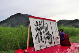 コウノトリが育つ湿地や山並みを前にパフォーマンスする書家の華汀さん=豊岡市城崎町今津 コウノトリが育つ湿地や山並みを前にパフォーマンスする書家の華汀さん=豊岡市城崎町今津