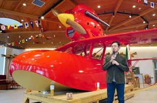 リニューアルされたカフェ「ロタンダ風ケ丘」で、映画「紅の豚」に登場する赤い飛行艇を再現した作品を紹介するジブリパークの宮崎吾朗監督=31日午前、愛知県長久手市