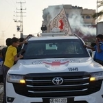 30日、パレスチナ自治区ガザ中部で、ハマスが引き渡した2人の遺体を乗せた赤十字車両を見る子どもたち(AP=共同)