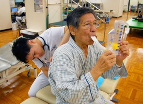 インセンティブ・スパイロメーターで呼吸訓練をする廣岡倭さん。理学療法士の牧浦大祐さんが呼吸音などをチェックする=神戸市中央区楠町7、神戸大病院 インセンティブ・スパイロメーターで呼吸訓練をする廣岡倭さん。理学療法士の牧浦大祐さんが呼吸音などをチェックする=神戸市中央区楠町7、神戸大病院