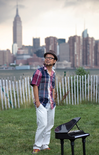 エンパイアステートビルが向こう岸に見える公園で、空を見上げる大江千里=ニューヨーク市ブルックリン