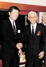 1964年の東京五輪実現に尽力したフレッド・和田勇さん(右)と握手する高杉良さん。「祖国へ、熱き心を」に結実した=1990年4月、東京・内幸町(高杉さん提供) 1964年の東京五輪実現に尽力したフレッド・和田勇さん(右)と握手する高杉良さん。「祖国へ、熱き心を」に結実した=1990年4月、東京・内幸町(高杉さん提供)