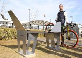 自転車をかけれらる馬車をモチーフにした形のベンチと、作者のケビン・ネルさん=福崎町福田 自転車をかけれらる馬車をモチーフにした形のベンチと、作者のケビン・ネルさん=福崎町福田