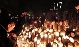 明かりに照らされる竹灯ろうの前で祈りを捧げる人たち=17日午前6時13分、神戸市中央区、東遊園地