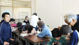 ボランティアに宿題を教えてもらう子どもたち。その様子を池田拓也先生(左端)が優しく見守る=西宮市高須町2 ボランティアに宿題を教えてもらう子どもたち。その様子を池田拓也先生(左端)が優しく見守る=西宮市高須町2