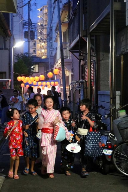 菓子でいっぱいになったかばんを提げ、地蔵盆で華やぐ路地を巡る子どもたち=神戸市長田区久保町3 菓子でいっぱいになったかばんを提げ、地蔵盆で華やぐ路地を巡る子どもたち=神戸市長田区久保町3