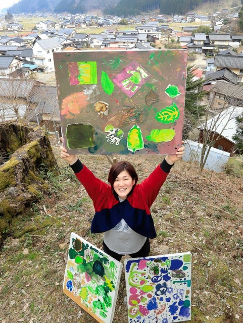 「アートを通して養蚕を伝えたい」。蔵垣地区を背に、子どもたちと桑を描いた絵を掲げる中島明日香さん=養父市大屋町蔵垣 「アートを通して養蚕を伝えたい」。蔵垣地区を背に、子どもたちと桑を描いた絵を掲げる中島明日香さん=養父市大屋町蔵垣
