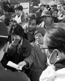ビル倒壊現場前で、警察官らに情報を求める人たち。顔写真の付いた書類を差し出す女性も=19日、西宮市甲子園口北町 ビル倒壊現場前で、警察官らに情報を求める人たち。顔写真の付いた書類を差し出す女性も=19日、西宮市甲子園口北町