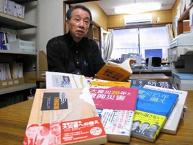 震災研が出版してきた本を手に、25年の活動を振り返る出口事務局長。「もうしばらく続けたい」=神戸市長田区 震災研が出版してきた本を手に、25年の活動を振り返る出口事務局長。「もうしばらく続けたい」=神戸市長田区