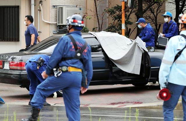 発砲事件があった現場を調べる捜査員ら。道路には血痕のようなものが見える=12日午前、神戸市長田区五番町