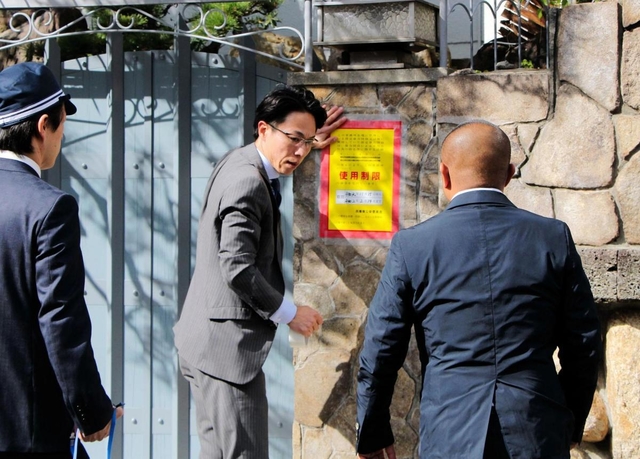 山口組の総本部で、使用制限を示す「標章」を仮命令用から本命令用に張り替える兵庫県警の警察官=15日、神戸市灘区篠原本町4