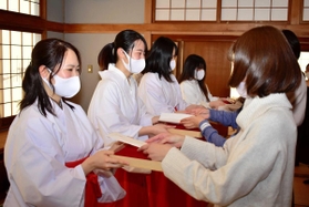 木の皿「折敷」に縁起物を載せて授与の練習をする巫女姿の学生ら＝明石市材木町