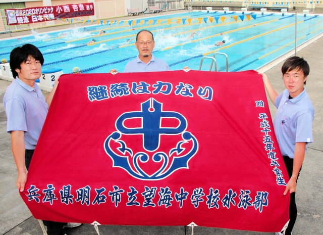 小西杏奈選手の在籍当時も使っていた望海中水泳部の部旗を手にする南谷昌宏さん（中央）ら＝明石市の同校