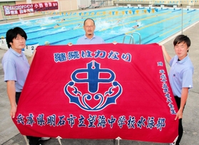 小西杏奈選手の在籍当時も使っていた望海中水泳部の部旗を手にする南谷昌宏さん（中央）ら＝明石市の同校