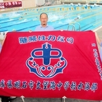 小西杏奈選手の在籍当時も使っていた望海中水泳部の部旗を手にする南谷昌宏さん（中央）ら＝明石市の同校