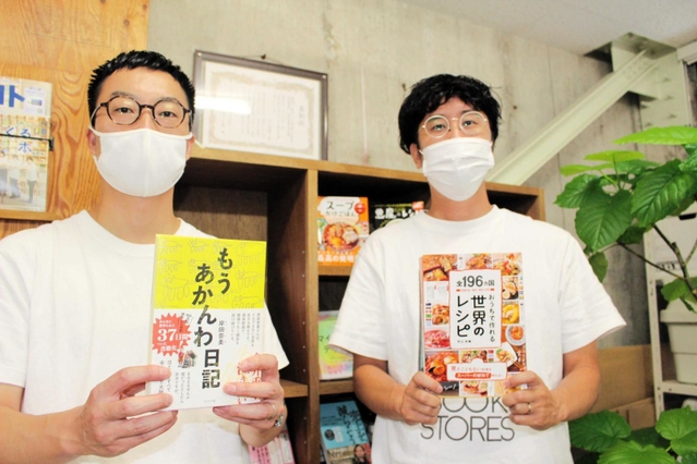 これまで出版した本を手にする社長兼編集長の大塚啓志郎さん（右）と社長兼営業責任者の高野翔さん＝明石市桜町