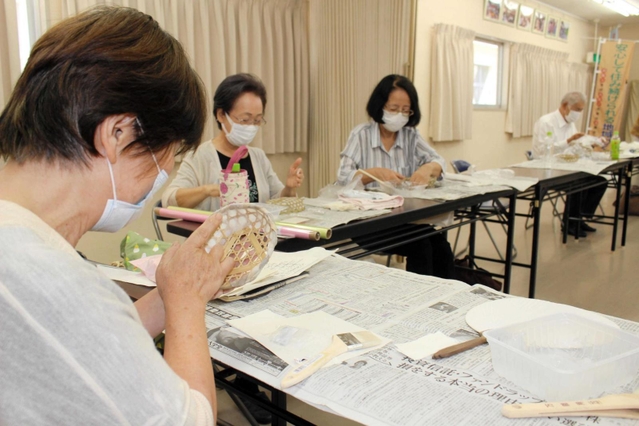 竹籠に和紙を張り付けるお年寄り＝明石市朝霧東町１