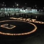 ろうそくの火で浮かび上がった「１・１７　ＢＥ　ＨＡＮＡＺＯＮＯ」を囲み、鎮魂の願いをささげる地域住民ら＝明石市西明石南町１