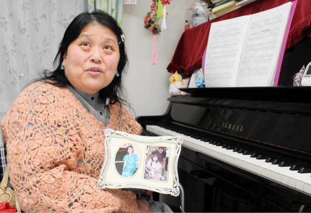 自宅のピアノ前で佐渡さんと写った写真を手に話す多久島さん＝明石市