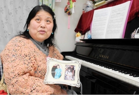 自宅のピアノ前で佐渡さんと写った写真を手に話す多久島さん＝明石市