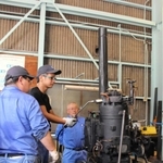 譲り受けた焼玉エンジンを試運転する金井清さん（奥）ら＝明石市港町７、明石発動機工作所