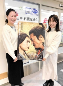 ポスターを手に明石城跡で撮影された映画をＰＲする明石観光協会の前川さん（左）と福田さん＝明石市東仲ノ町