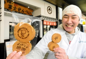 「お世話になりました」の焼き印入りせんべいを手にする富士の山菓舗７代目の原田岳秋さん。「愛」の焼き印入りはバレンタインデーやホワイトデーの贈り物にぴったりという＝明石市本町１