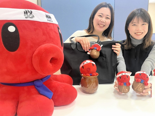 「パパたこ」と「ひっぱりだこ飯」のコラボぬいぐるみストラップを手にＰＲする明石観光協会職員＝明石市東仲ノ町