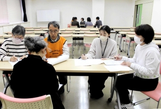 被災者役（手前）から生活環境などを聞き取る参加者たち＝明石市貴崎１