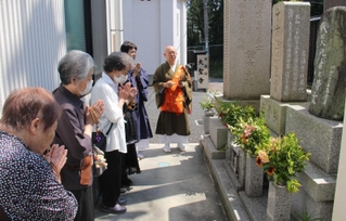 空襲犠牲者の墓の前で手を合わせる参列者ら。奥は松尾義康住職＝大聖寺