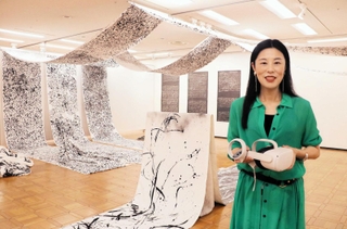 会場でＶＲのヘッドセットを手に作品について語る岩坂典子さん＝明石市立文化博物館