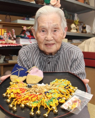 草履のお守りを編んでいる野瀬田いくゑさん。後方の棚には陶芸の作品が並ぶ＝明石市二見町福里