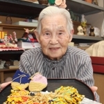 草履のお守りを編んでいる野瀬田いくゑさん。後方の棚には陶芸の作品が並ぶ＝明石市二見町福里