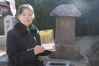 善楽寺の碑の前で著書を持つ義根益美さん＝明石市大観町