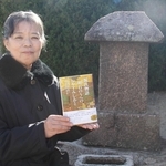 善楽寺の碑の前で著書を持つ義根益美さん＝明石市大観町