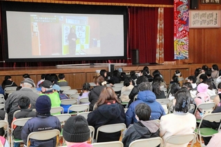 地域住民らが阪神・淡路大震災の体験を語る動画を見る子どもや保護者ら＝江井島小学校