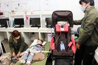 訓練で、明石医療センターから医療機器への電源の供給を受ける太田メリサさん（中央）と家族＝明石市大久保町八木